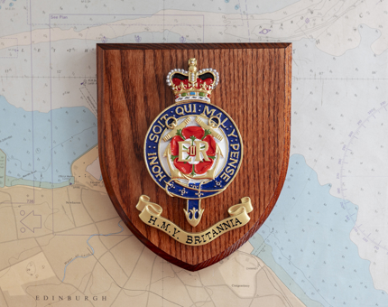 A Britannia crest on a wooden plaque. It is sitting on a map. 