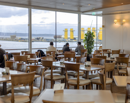 Visitors sitting at tables in the Royal Deck Tearoom on Britannia looking at the view over the Port of Leith. 