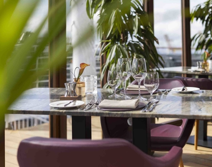 a table is set for dinner in The Lighthouse Restaurant. There are plants by the window and in the foreground. 