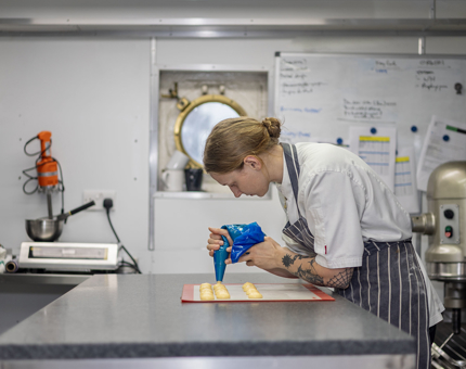 A chef in the Galley aboard The Royal Yacht Britannia piping choux pastry onto trays. 