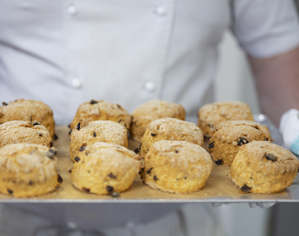 A chef is holding a tray of fruit scones straight out of the oven. 