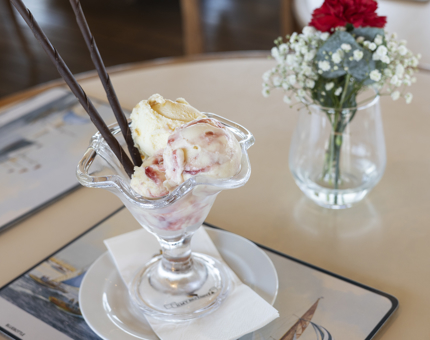 A bowl of ice cream in the Tearoom, there is also a vase with a red carnation and white baby's breath flowers in it. 