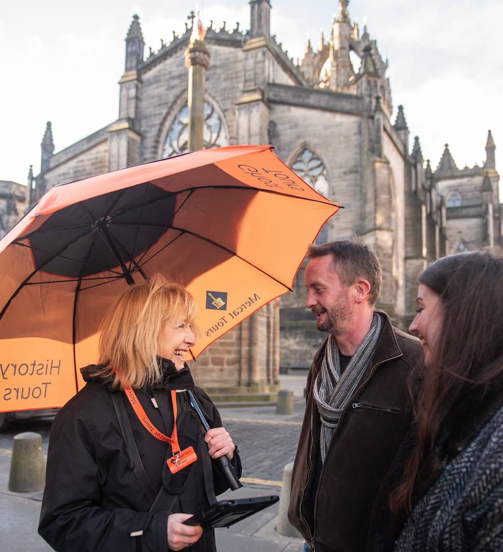 A lady with an orange umbrella speaking to two people outside St.Gile's Cathedral in Edinburgh.