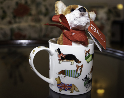 Toy corgi dog sitting in a mug decorated with dogs wearing jumpers.