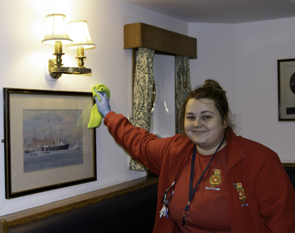 Housekeeper dusts a watercolour picture of The Royal Yacht Britannia.