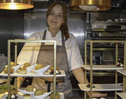 Chef stands in front of tiered Afternoon Tea stand containing miniature savoury treats.