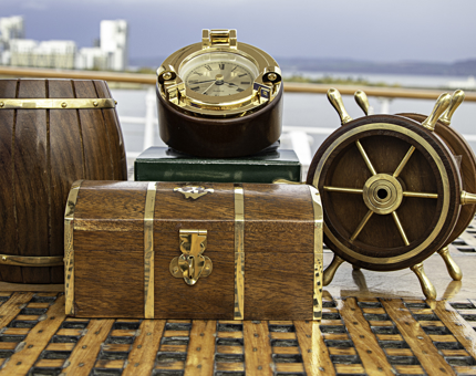 Two moneyboxes in the shape of a ship's barrel and treasure chest, a porthole-shaped clock and ships' wheel containing drinks coasters.