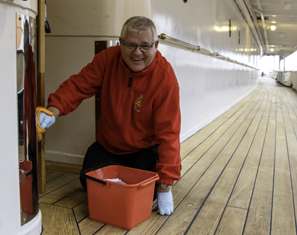 Housekeeper man wipes door of the Galley on deck.