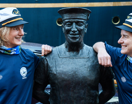 Olympians Sarah Winckless and Dame Katherine Grainger pose next to the statue of longest serving Royal Yachtsman, Norrie.