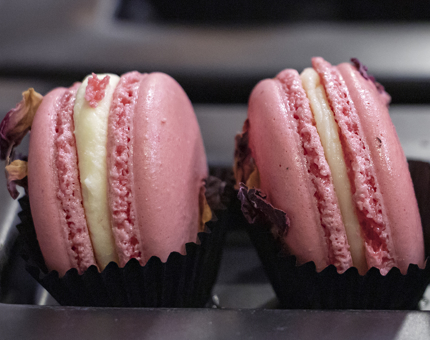 Two pink rose flavoured macarons sitting on a plate.