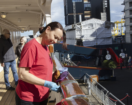 A woman polishing a teak handrail on the Shelter Deck on Britannia.