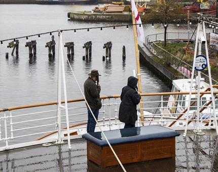 Two visitors are listening to the audio tour as they are standing outside on deck.