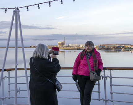 One visitor standing posing with the Firth of Forth in the background as another visitor is taking her photo.