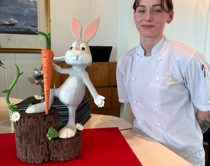 A large decorative cartoon-like Easter Bunny sculpture sits on the piano in the Royal Deck Tea Room. Chef Amelia who created the design, standing next to the sculpture.