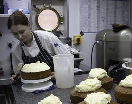 A Pastry Chef icing a carrot cake in the Galley.