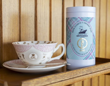A cup and saucer commemorating 100 years since Queen Elizabeth II's birth and a tin of tea wrapped in a tartan label. 