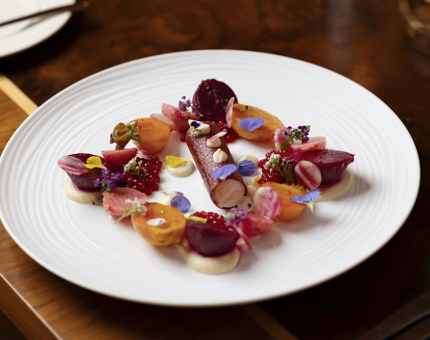 A white plate with a heritage beetroot salad on it, it is colourful with reds and orange colours, there are small flowers garnishing the dish. 