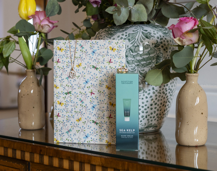 A table with vases of flowers, displaying a note book, hand cream and a necklace from the Shop. 