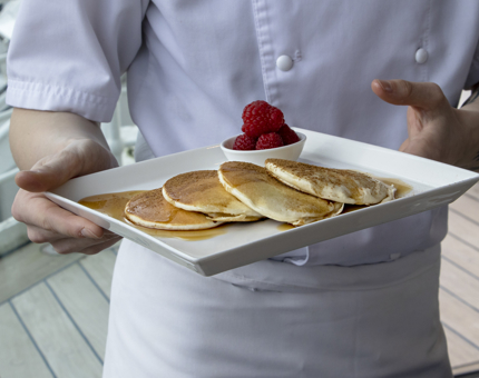 A chef is holding a plate with pancakes and raspberries on it.
