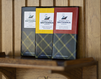 Three bars of chocolate sitting on a wooden shelf, leaning against a wood paneled wall.
