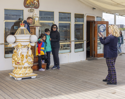 A visitor assistant is taking a photo of a a family at Britannia's Bell in the Port of Leith. 
