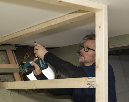 A Maintenance man drilling into a wooden frame in a room aboard Fingal in Leith. 