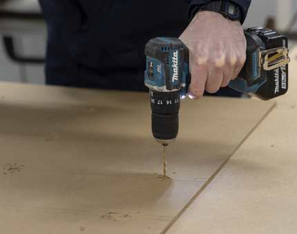A hand holding a power drill to manufacture pigeon hole storage. 