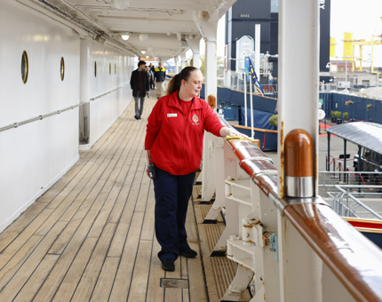 A Housekeeper is wiping down the handrails along one of Britannia's decks. 