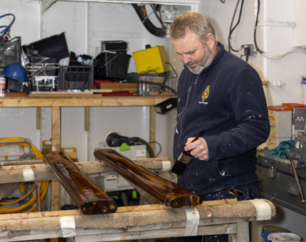A Maintenance man varnishing a handrail. 