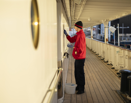 A Housekeeper in on the deck polishing the brass portholes. 