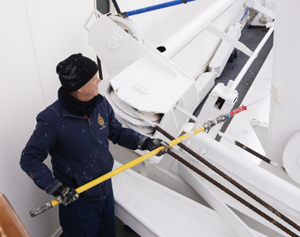 A Maintenance man is holding a long handled paint roller, Painting a Davit white At The Onboard Garage. 
