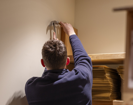 A maintenance man is installing the shelves in the Shop's storage area. 