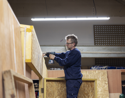 A Maintenance team member using a power drill to build and enclosed area in a workshop. 