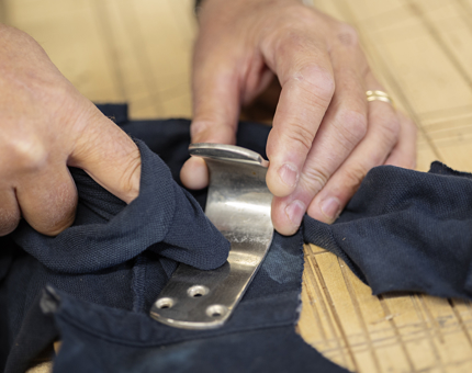 Two hands with a blue rag polishing a metal bracket. 