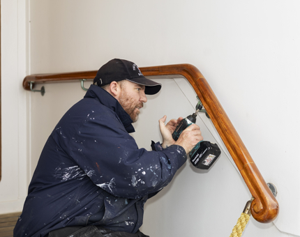 A Maintenance man is reattaching a hand rail back in place after restoration. 