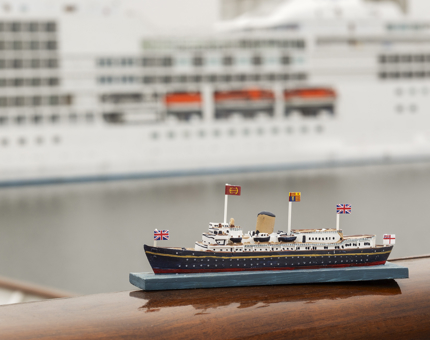 A model of Britannia sitting on the railing, there is a cruise ship in the background. 