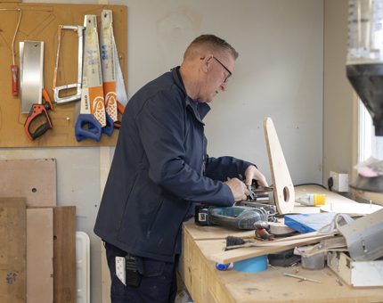 A Maintenance man is at a workbench making alterations to a router for a porthole template for an office door. 