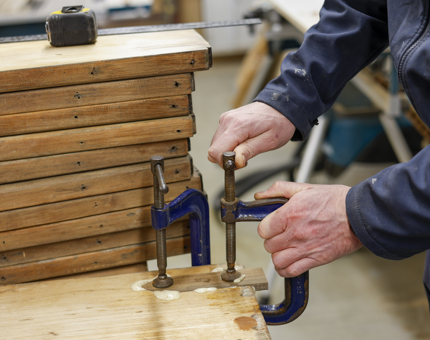 A Maintenance man is clamping together a set of wooden pieces. 