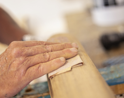 A close up of a hand sanding a wooden handrail. 