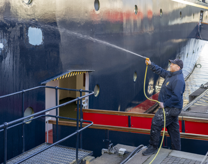 A maintenance team member is holding a hose, washing down the side of Britannia. 