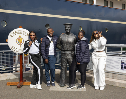 Four visitors stand next to a statue of a Royal Yachtsman on the Quayside next to Britannia. 
