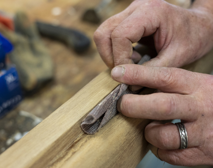 A close up of hands sandning a wooden handrail. 