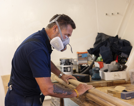 A Maintenance man is in the workshop sanding handrails from Britannia. 