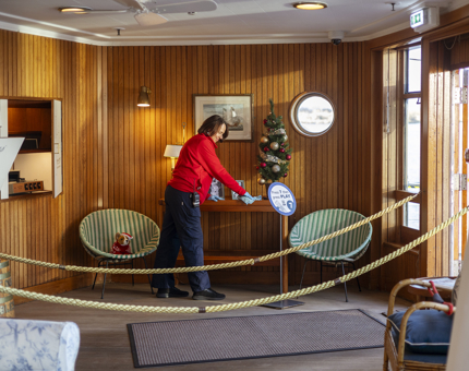 In the Sun Lounge aboard The Royal Yacht Britannia, a Housekeeper is cleaning a table. 