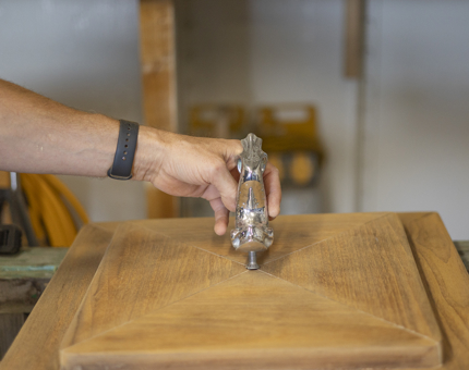 A hand holding a silver dolphin fish on top of wooden top. 