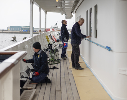 Three Maintenance team members on the deck painting the walls white. 