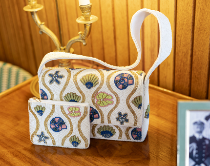 A beaded bag and purse decorated with seashells sit on a wooden table. 