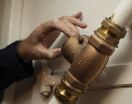 A hand is adding a valve onto a brass fixture on a pipe. 