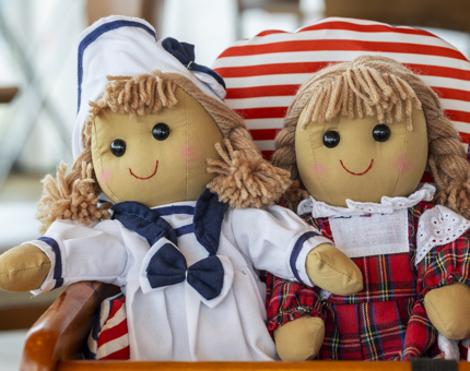 Two soft dolls. One is wearing a sailor's outfit, the other is wearing a red tartan dress.