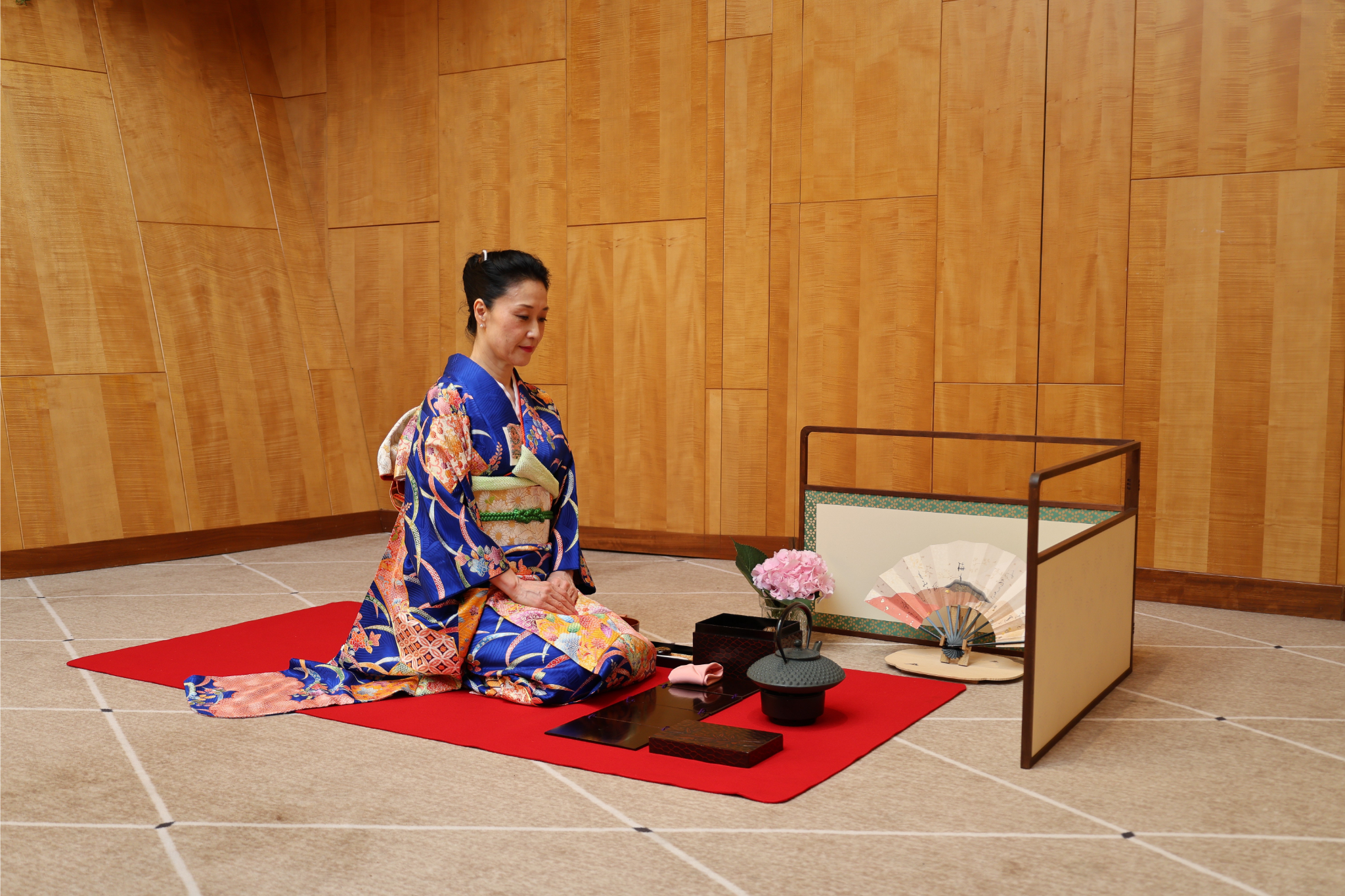 A woman wearing a Japanese Kimono is kneeling on a red carpet with tea making items in front of her aboard Fingal in the Port of Leith.